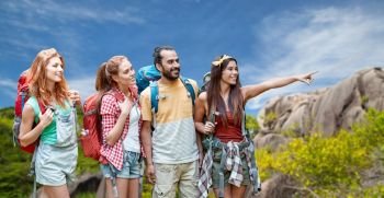 travel, tourism, hike and adventure concept - group of smiling friends with backpacks pointing finger to something over background of seychelles island. friends with backpacks over seychelles island 