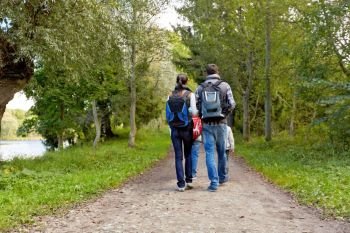 family, tourism and hiking concept - happy mother, father, son and daughter with backpacks walking in woods. family with backpacks hiking or walking in woods