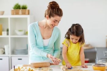 family, cooking and people concept - happy mother and little daughter with molds making cookies from dough at home kitchen. happy mother and daughter making cookies at home