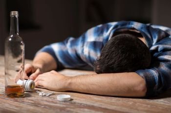 suicide, depression and overdose concept - dead man with bottle of alcohol and pills lying on table at night. dead man overdosed on pills with alcohol