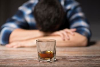 alcoholism, alcohol addiction and people concept - male alcoholic with glass of whiskey lying or sleeping on table at night. drunk man with glass of alcohol on table at night