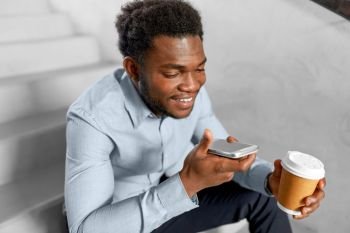 business, communication and technology concept - african american businessman calling or using voice recorder on smartphone at coffee break on office stairs. businessman records voice by smartphone at office