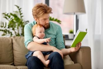 family, fatherhood and people concept - red haired father reading book for little baby daughter at home. father reading book for baby daughter at home