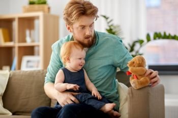 family, fatherhood and people concept - happy red haired father and little baby daughter playing with teddy bear at home. father and baby daughter with teddy bear at home