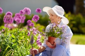 gardening and people concept - happy senior woman planting flowers at summer garden. senior woman planting flowers at summer garden