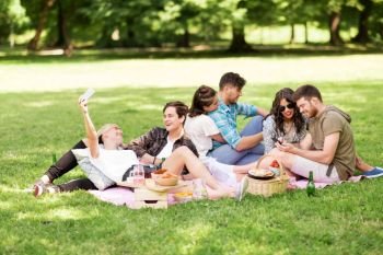 friendship, leisure, technology and people concept - group of friends with smartphones and non alcoholic beer chilling on picnic blanket at summer park. friends with smartphones on picnic at summer park