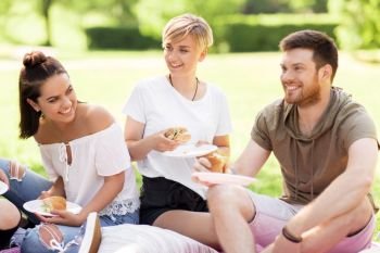 friendship, leisure and fast food concept - group of happy friends eating sandwiches or burgers at picnic in summer park. happy friends eating sandwiches at summer picnic