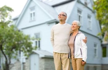 old age, accommodation and real estate concept - happy senior couple hugging over house background. happy senior couple hugging over house background