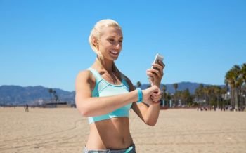 sport, technology and healthy lifestyle concept - smiling young woman with fitness tracker and smartphone exercising over venice beach background in california. happy woman with fitness tracker and smartphone