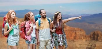 travel, tourism, hike and adventure concept - group of smiling friends with backpacks pointing finger to something over grand canyon national park background. group of friends with backpacks at grand canyon