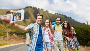 technology, travel, tourism, hike and people concept - group of smiling friends with backpacks taking selfie by smartphone over big sur of california hills background. friends with backpack taking selfie by smartphone