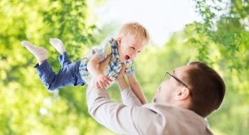 family, childhood, fatherhood and people concept - happy father and little son playing and having fun over green natural background. father with son playing and having fun in summer