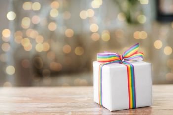homosexual and lgbt concept - gift box with gay pride awareness ribbon on wooden table over festive lights background. present with gay awareness ribbon on table
