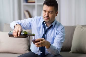 alcoholism, alcohol addiction and people concept - male alcoholic pouring red wine to glass at home. alcoholic pouring red wine to glass at home