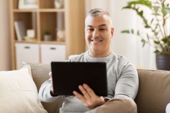 technology, people and lifestyle concept - man with tablet pc computer sitting on sofa at home. man with tablet pc sitting on sofa at home