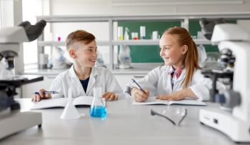 education, science and children concept - happy smiling kids with workbooks studying chemistry at school laboratory and talking. happy kids studying chemistry at school laboratory