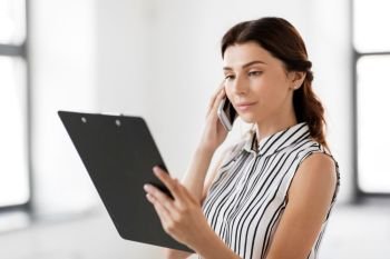 business people, technology and corporate concept - businesswoman or realtor with clipboard calling on smartphone at office. businesswoman calling on smartphone at office