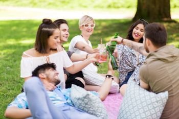leisure, people and celebration concept - happy friends clinking non alcoholic drinks at picnic in summer park. friends clinking drinks at picnic in summer park