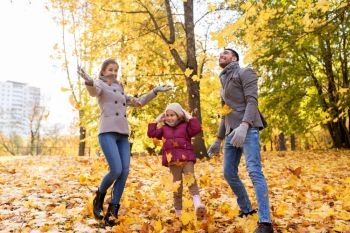 family, season and people concept - happy mother, father and little daughter playing with autumn leaves at park. happy family playing with autumn leaves at park