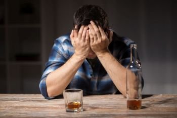 alcoholism, alcohol addiction and people concept - male alcoholic with bottle and glass drinking whiskey at night. alcoholic with bottle drinking whiskey at night