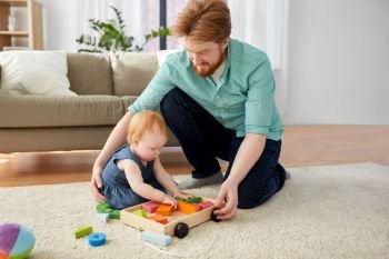 family, fatherhood and people concept - happy red haired father and little baby daughter playing with toy blocks kit at home. father and baby playing with toy blocks at home