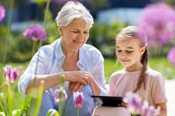 family, leisure and technology concept - happy grandmother and granddaughter with tablet pc computer at summer garden. grandmother and girl with tablet pc at garden