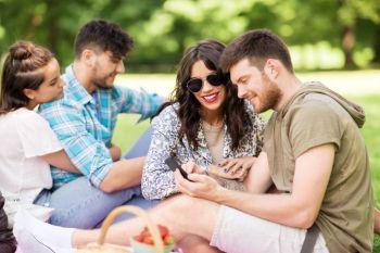 friendship, leisure, technology and people concept - group of friends with smartphones chilling on picnic blanket at summer park. friends with smartphones on picnic at summer park