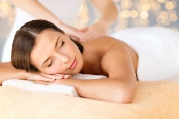 wellness, spa and beauty concept - close up of beautiful woman having massage over holidays lights background. close up of beautiful woman having massage at spa