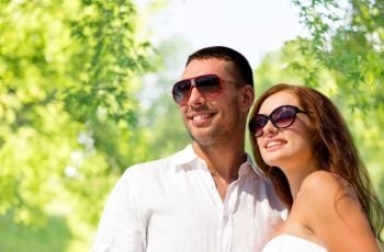 love, summer and relationships concept - happy smiling couple in sunglasses over green natural background. happy smiling couple in sunglasses