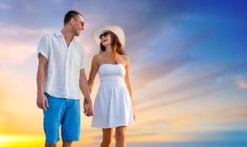 love, summer and relationships concept - happy couple on vacation wearing sunglasses and walking holding hands over evening sky background. happy couple on vacation walking holding hands