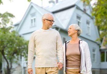 old age, accommodation and real estate concept - happy senior couple holding hands over living house background. happy senior couple holding hands over house