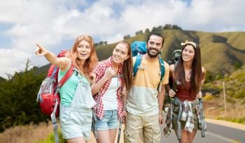 adventure, travel, tourism, hike and people concept - group of smiling friends with backpacks pointing finger over big sur hills of california background. group of friends with backpacks over big sur hills