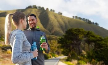 fitness, sport and people concept - smiling couple with bottles of water over big sur hills background in california. couple of sportsmen with water over big sur hills