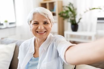 technology, communication and people concept - happy smiling senior woman in glasses taking selfie at home. smiling senior woman taking selfie at home