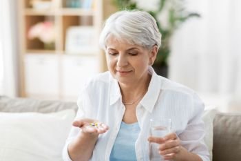 age, medicine, healthcare and people concept - senior woman with glass of water taking pills at home. senior woman with water taking medicine at home
