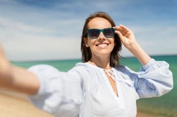 summer holidays and leisure concept - happy smiling woman in sunglasses taking selfie on beach. woman in sunglasses taking selfie on summer beach