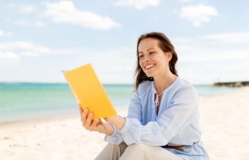people and leisure concept - happy smiling woman reading book on summer beach. happy smiling woman reading book on summer beach