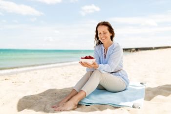 people and leisure concept - happy smiling woman with strawberries on summer beach. happy woman with strawberries on summer beach