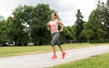 fitness, sport and healthy lifestyle concept - smiling woman with earphones running at park and listening to music. woman with earphones running at park
