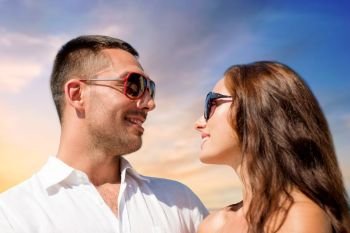 love, summer and relationships concept - happy smiling couple in sunglasses over sky background. happy couple in sunglasses over sky background