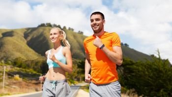 fitness, sport and healthy lifestyle concept - smiling couple with heart-rate watch running over big sur hills and road background in california. smiling couple running over big sur hills