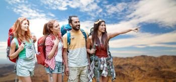 travel, tourism, hike and adventure concept - group of smiling friends with backpacks pointing finger to something over grand canyon national park hills background. group of friends with backpacks over mountains