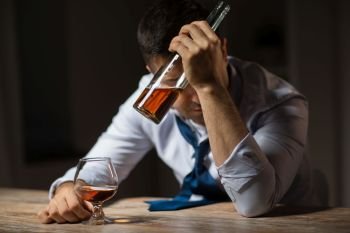 alcoholism, alcohol addiction and people concept - male alcoholic with bottle drinking brandy at table at night. drunk man drinking alcohol at table at night