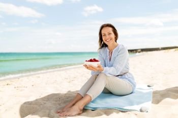 people and leisure concept - happy smiling woman with strawberries on summer beach. happy woman with strawberries on summer beach