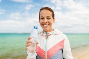 fitness, sport and healthy lifestyle concept - woman drinking water after exercising on beach. woman drinking water after exercising on beach