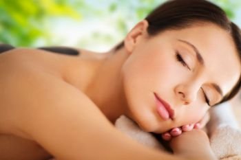 wellness, spa and beauty concept - close up of beautiful woman having hot stone therapy over green natural background. beautiful woman having hot stone therapy at spa