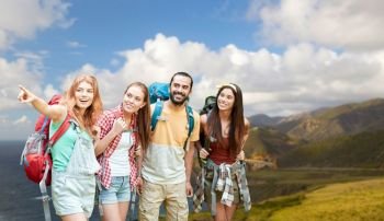 adventure, travel, tourism, hike and people concept - group of smiling friends with backpacks pointing finger over bixby creek bridge on big sur coast of california background. group of friends with backpacks on big sur coast