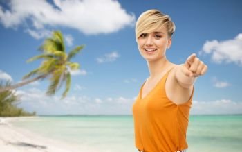 travel, tourism and summer holidays concept - happy smiling young woman over exotic tropical beach with palm trees background pointing at you. smiling young woman pointing at you