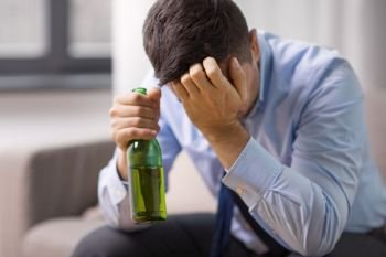 alcoholism, alcohol addiction and people concept - male alcoholic drinking beer from bottle at home. male alcoholic drinking beer at home