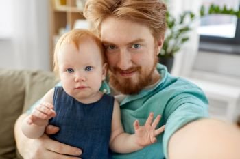 family, fatherhood and people concept - happy red haired father with little baby daughter taking selfie at home. happy father with baby taking selfie at home